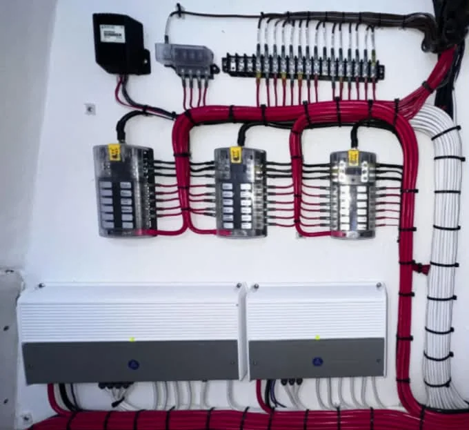 A marine electrical panel with three fuse distribution boxes and neatly loomed red and white wiring.