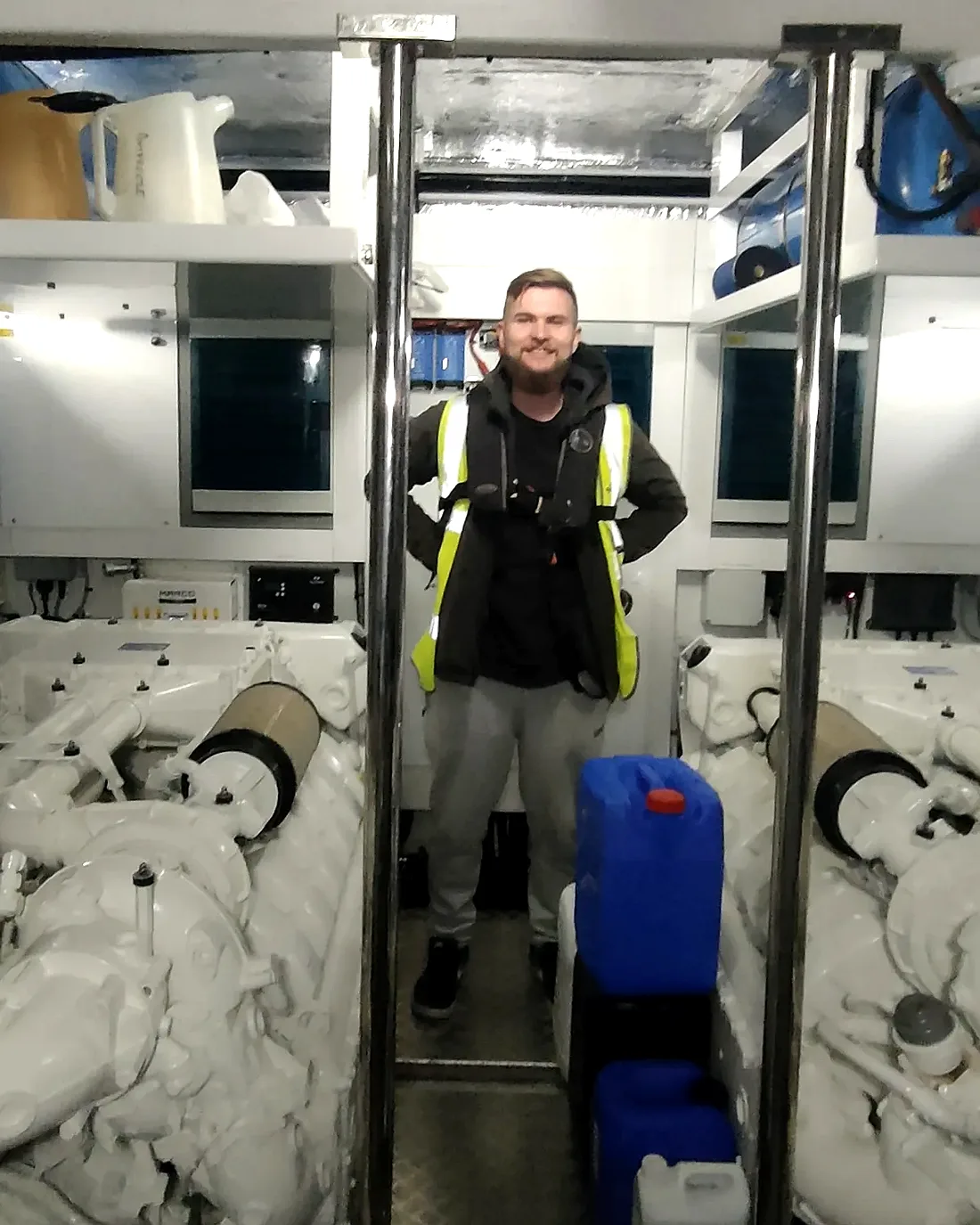 Adam Puchowicz in high-visibility kit, standing between the two main engines in a yacht engine room.